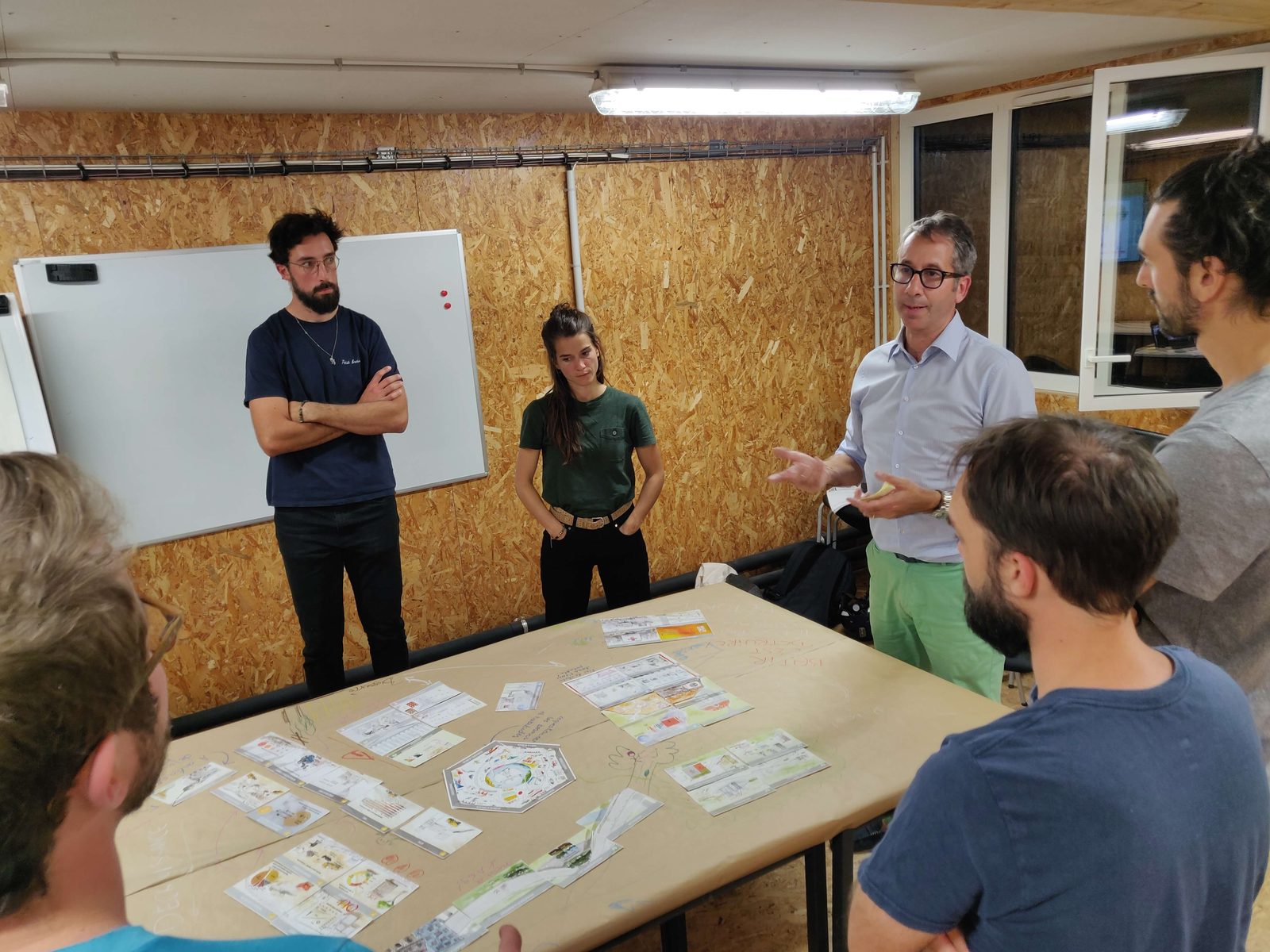Atelier Fresque de la Construction animé par FedeA Atelier Fresque de la Construction : participants autour des cartes reliées sur une grande table, l'animateur échange avec le groupe